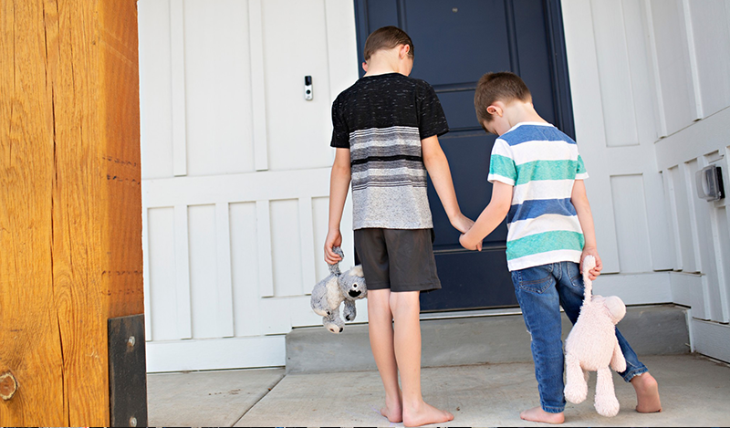 two boys with stuffed animals hold hands before going inside (no children's faces visible)