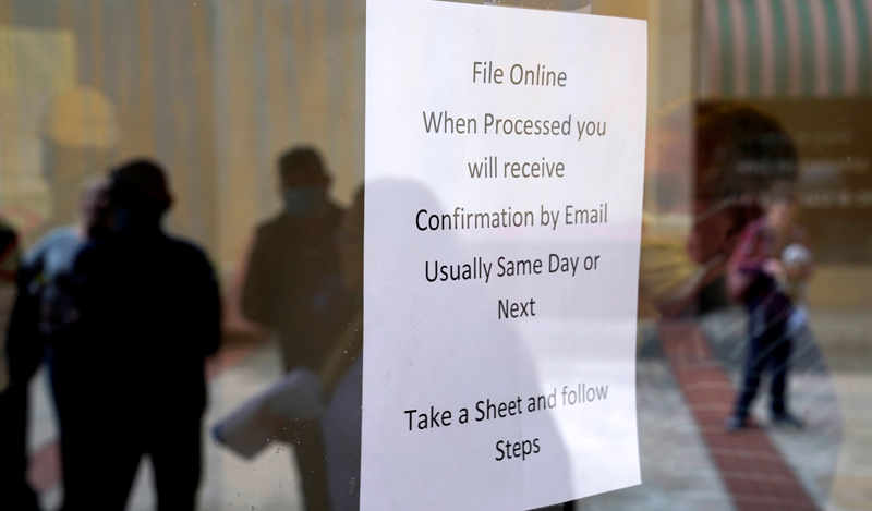 People who lost their jobs are reflected in the door of an Arkansas Workforce Center as they wait in line to file for unemployment following an outbreak of the coronavirus disease (COVID-19), in Fort Smith, Arkansas, U.S. April 6, 2020. REUTERS/Nick Oxford