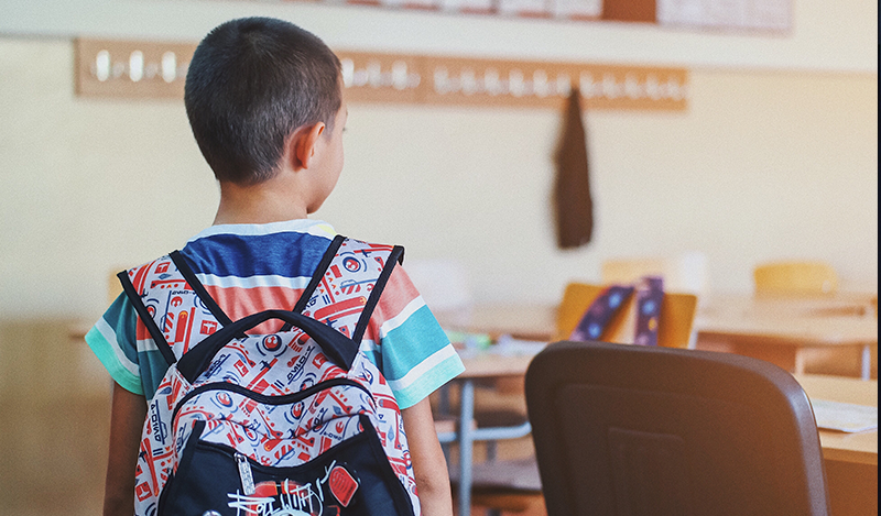 A young male student wearing a backpack looks for a seat in a classroom